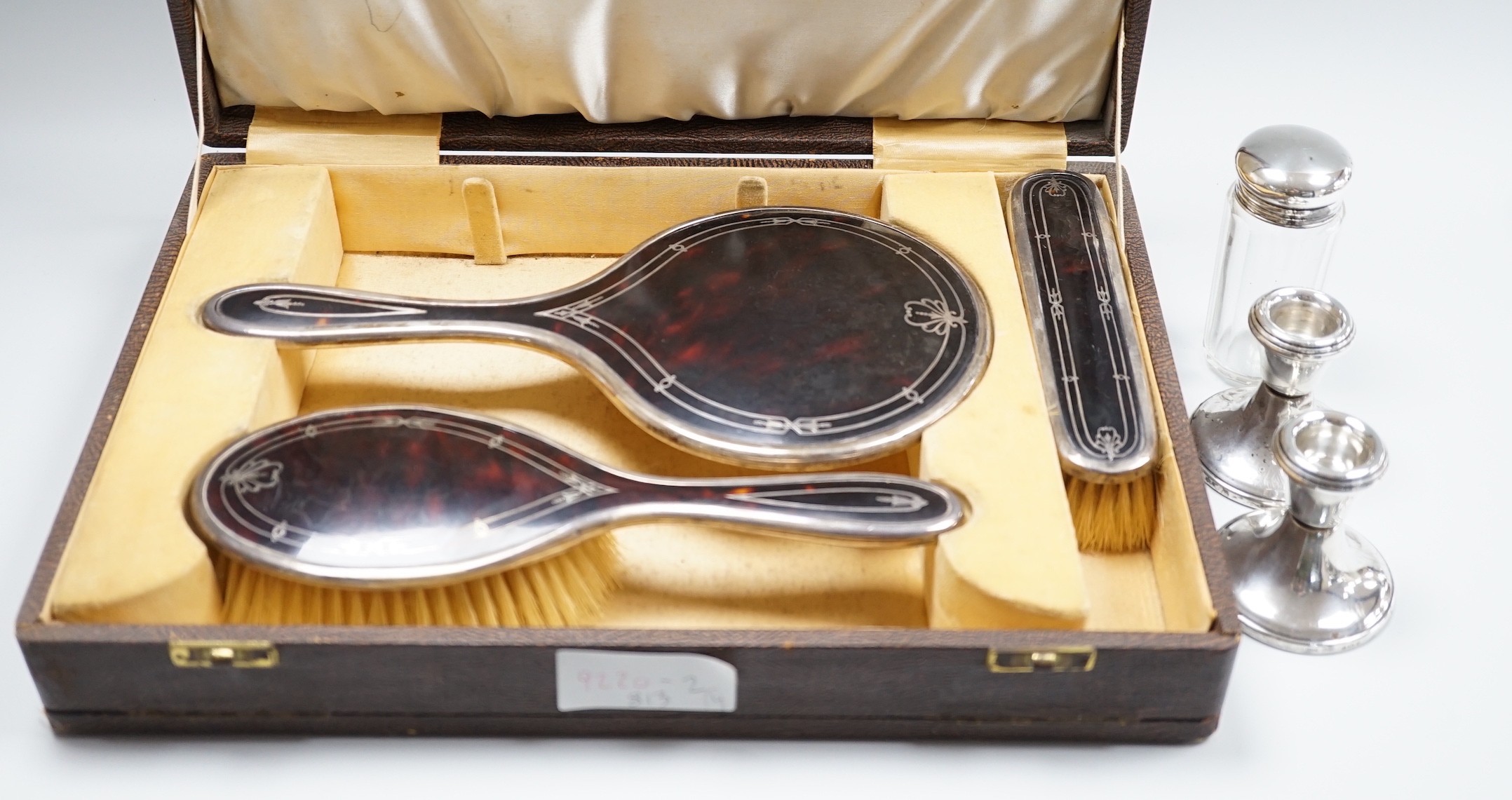 A George V cased three piece silver and tortoiseshell pique mounted mirror and brush set (lacking comb), Walker & Hall, Birmingham, 1931/37, a pair of modern silver mounted dwarf candlesticks and a silver mounted glass t